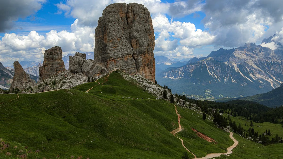 Stunning view of Cinque Torri, Dolomites with green meadows and cloudy sky.